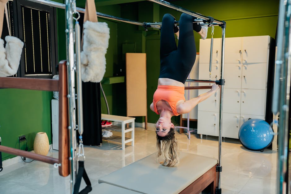 Adult woman doing an upside-down pose on a reformer pilates machine in a fitness studio.